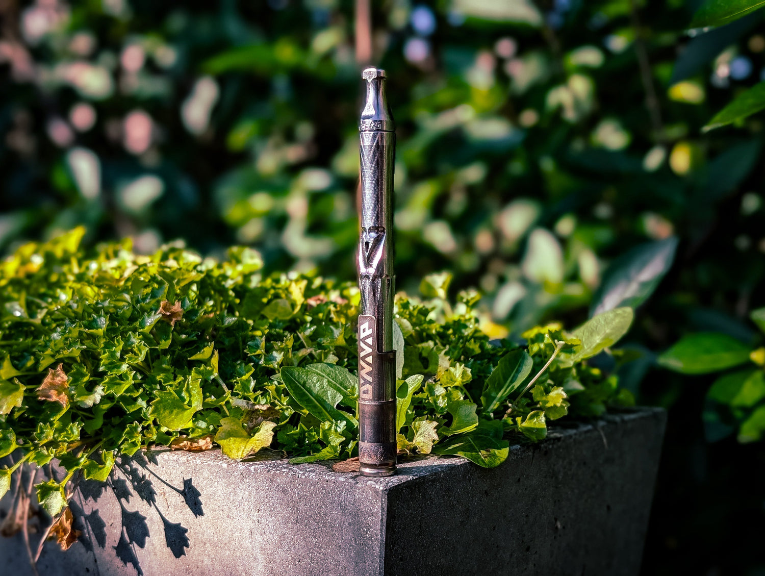DynaVap vaporizer on concrete planter with greenery